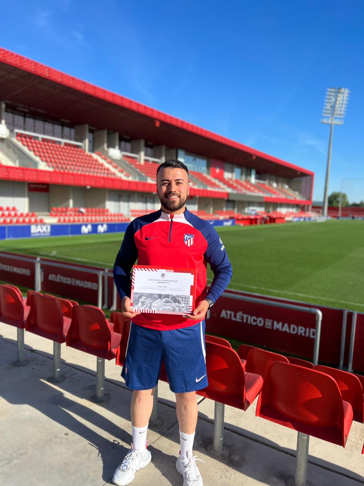 Ein lachender Mann mit Bart in Atletico Madrid Kleidung hält ein Zertifikat im Stadion