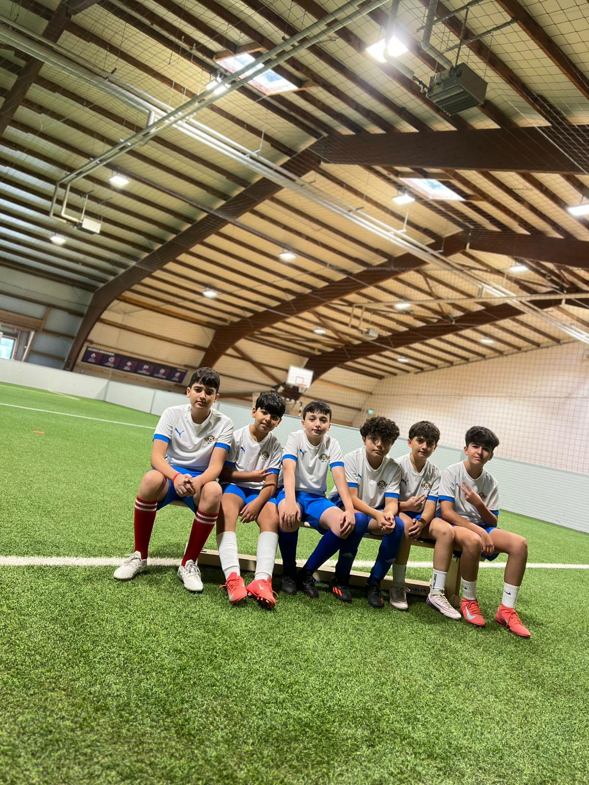 Sechs Jungen in weißen Trikots sitzen entspannt auf einer Bank in einer Sporthalle