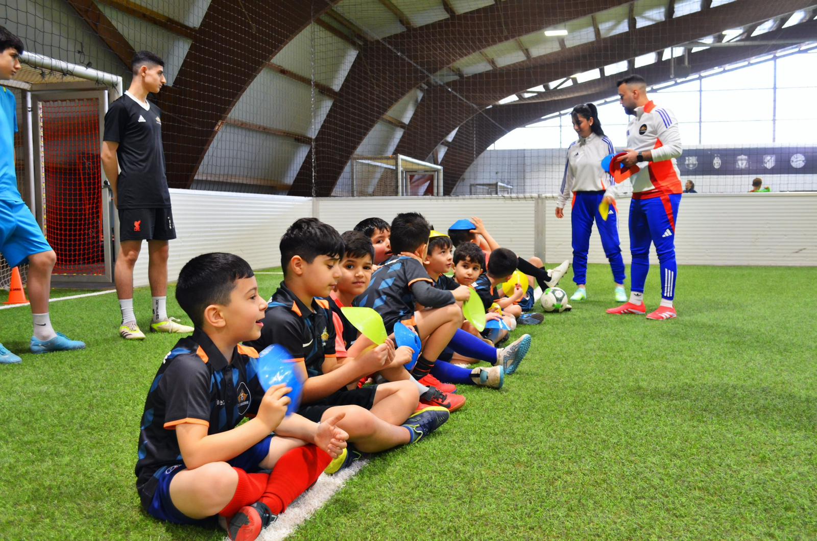 Eine Gruppe von Jungen sitzt lachend auf grünem Kunstrasen in einer Fußballhalle