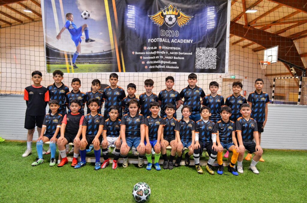 Eine Jugendfußballmannschaft posiert lächelnd in schwarzer Ausrüstung in der Halle