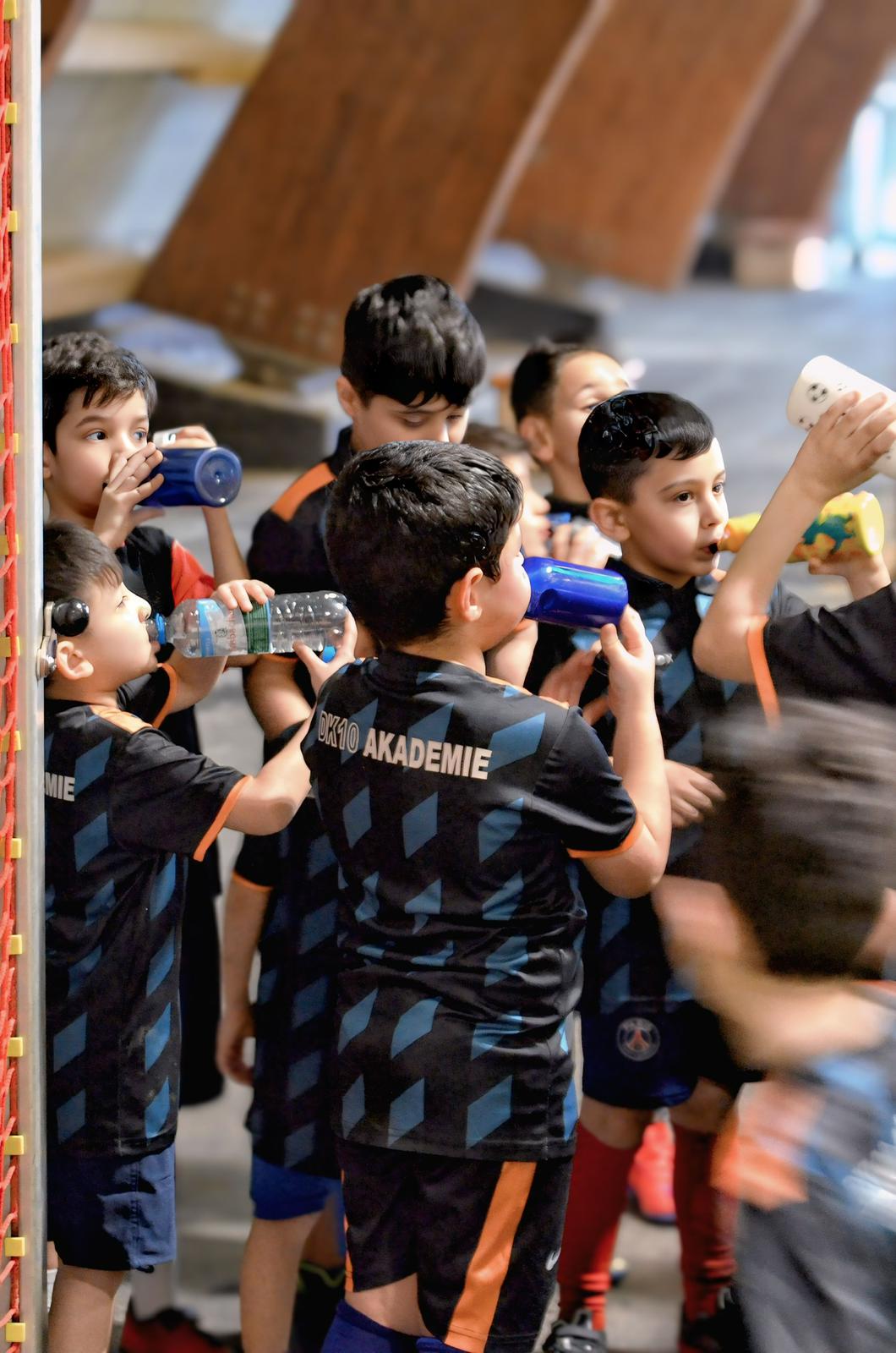 Mehrere Jungen in schwarzen Sporttrikots trinken lachend Wasser in einer Halle