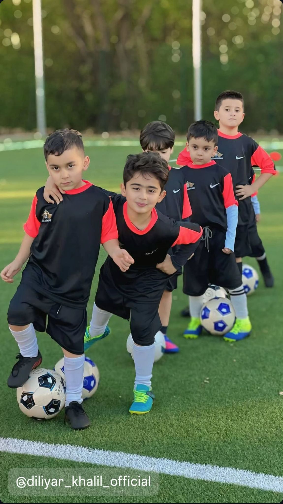 Fuenf Jungen mit schwarzen und roten Trikots stehen lachend auf dem Fussballfeld