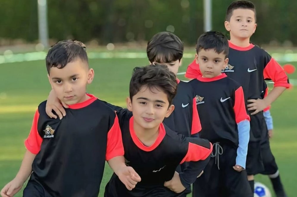 Fünf Jungen mit dunklen Haaren und schwarzen Trikots posieren fröhlich auf dem Fußballfeld